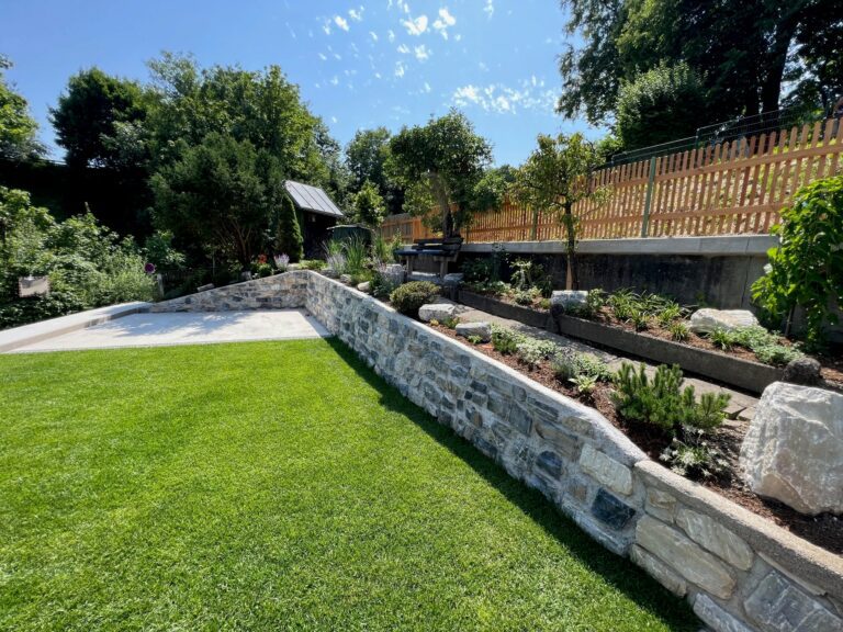 Gepflegter Garten mit Rasenfläche, Steinmauern und Pflanzbeeten unter blauem Himmel