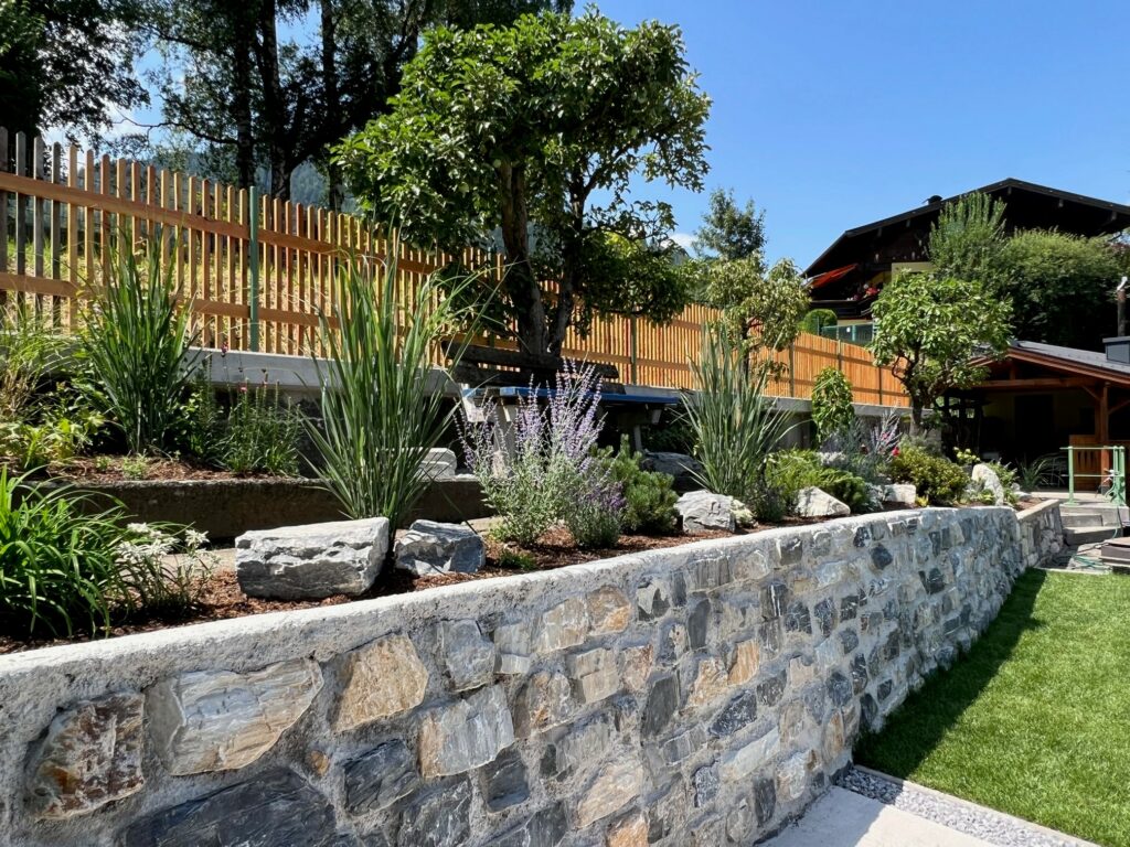 Ein gepflegter Garten mit Steinmauer, Pflanzen und einem Holzzaun im Hintergrund