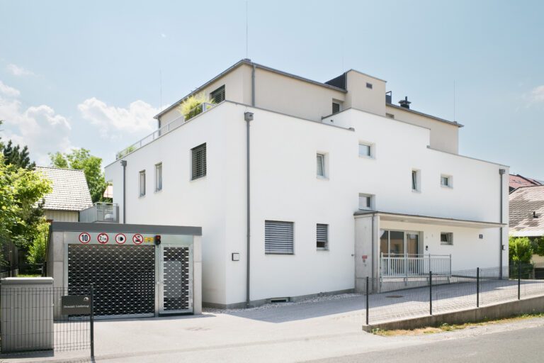 Modernes weißes Wohngebäude mit flachem Dach und umzäuntem Eingangsbereich