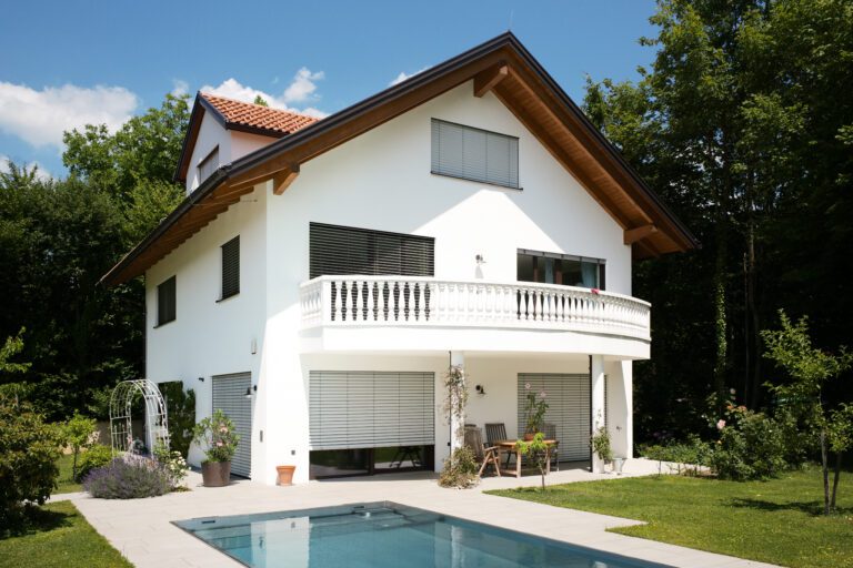 Modernes weißes Einfamilienhaus mit Pool und Garten an einem sonnigen Tag