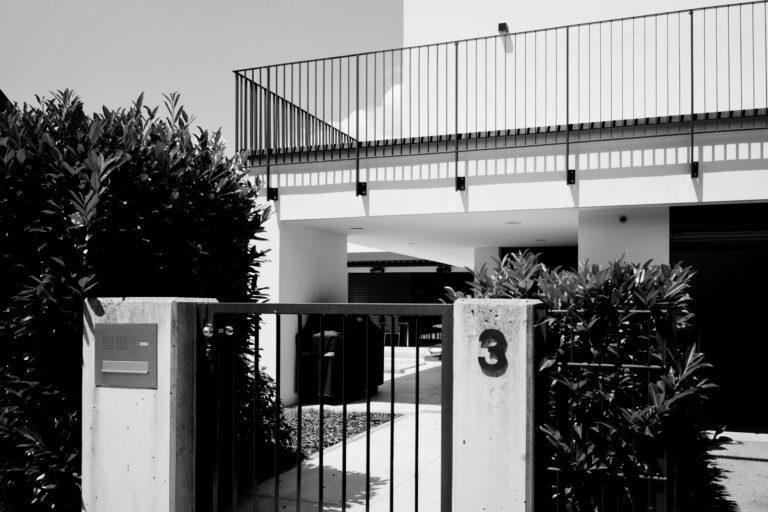 Schwarz-Weiß-Aufnahme einer modernen Gebäudefassade mit Eingangstor, an dem die Nummer 3 befestigt ist