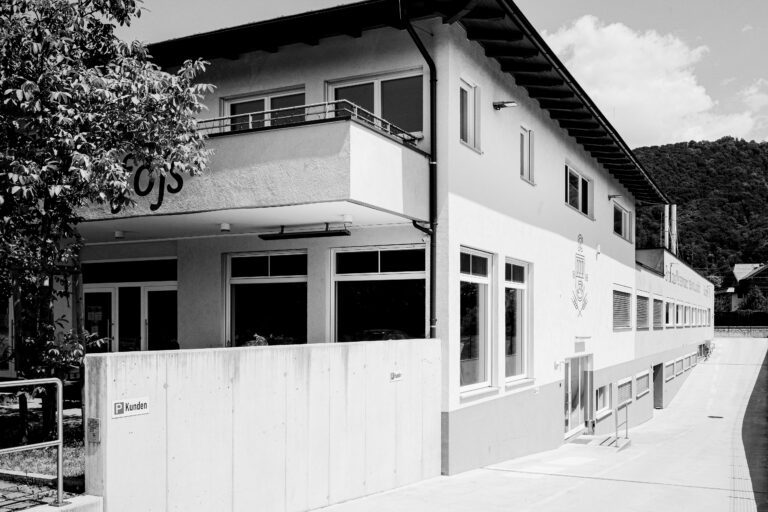 Schwarz-weiß Aufnahme eines modernen Gebäudes mit Schild 'Kundenparkplatz' im Vordergrund