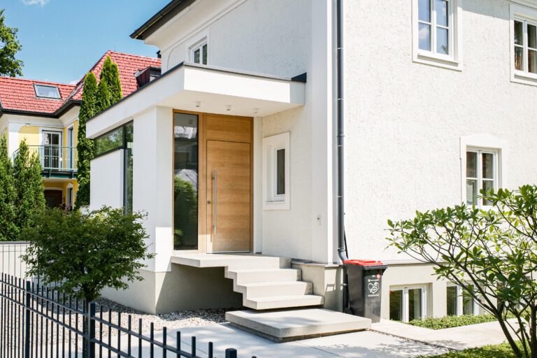 Moderne Haustür eines Einfamilienhauses mit Stufen und Pflanzen im Vorgarten