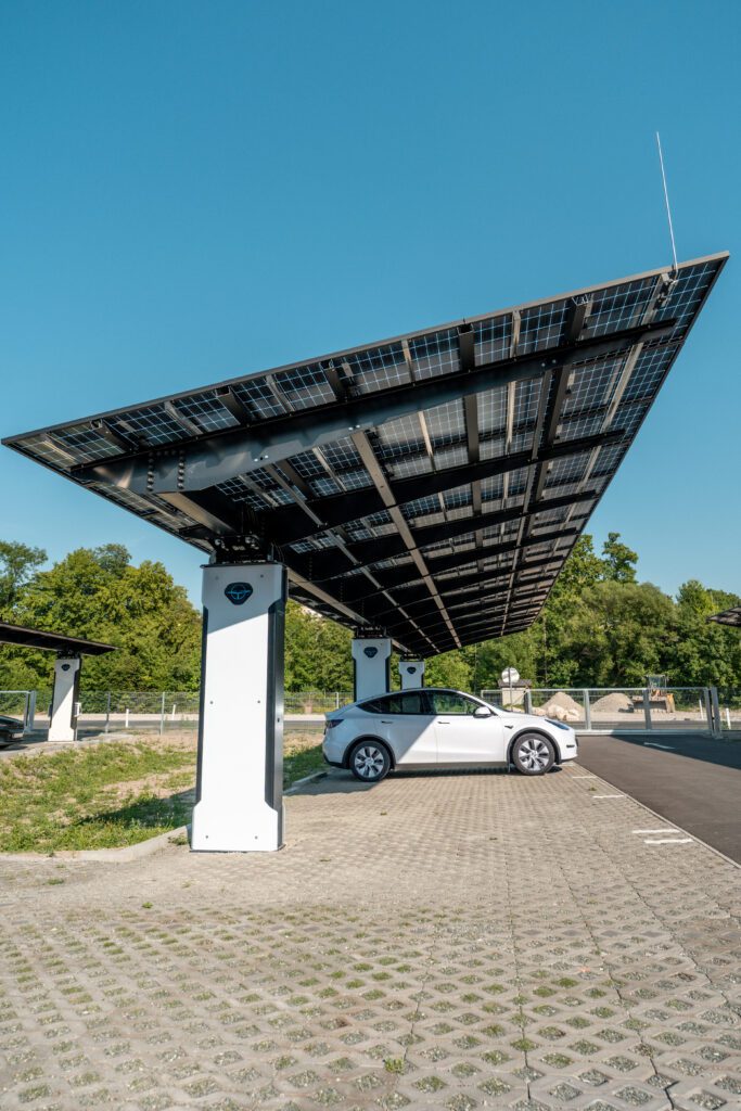 Ein weißes Elektroauto lädt an einer solarbetriebenen Ladestation an einem sonnigen Tag.