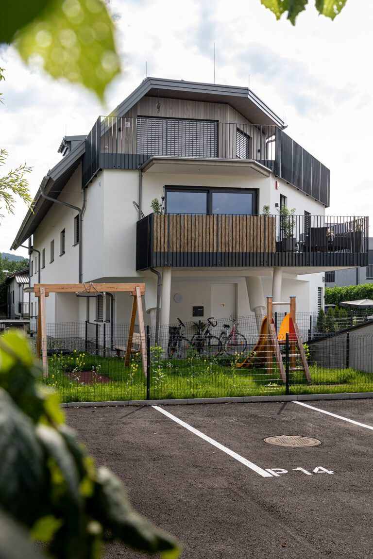 Ein modernes zweistöckiges Wohnhaus mit Balkon, umgeben von Grünanlagen und Fahrrädern im Vordergrund.