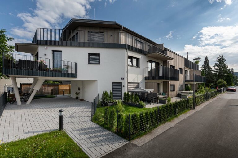 Modernes Mehrfamilienhaus mit Balkonen, begrünten Außenanlagen und einer Einfahrt